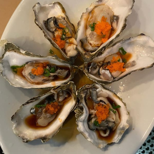 Six fresh oysters on the half shell, topped with bright orange tobiko and green onions.