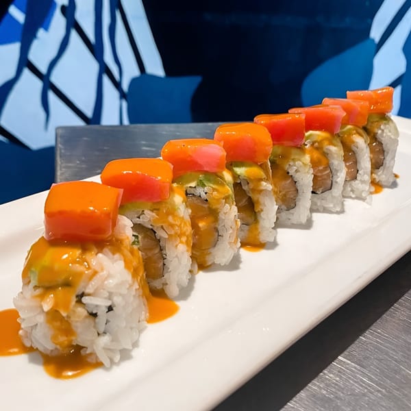 Sushi 4 Reel's vibrant sushi rolls topped with orange fish and drizzled with sauce on a white plate.