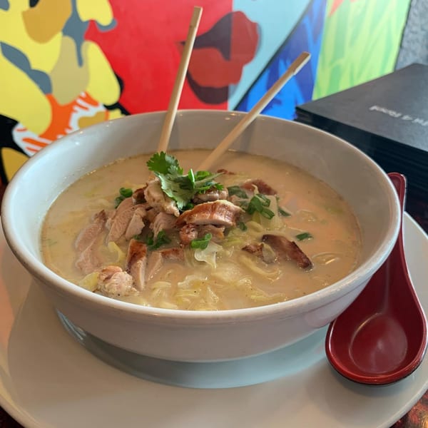 Creamy chicken ramen with chopsticks and a red spoon, against a colorful abstract background.