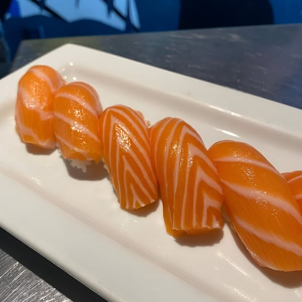 Five pieces of fresh salmon nigiri sushi with white rice on a rectangular white plate.