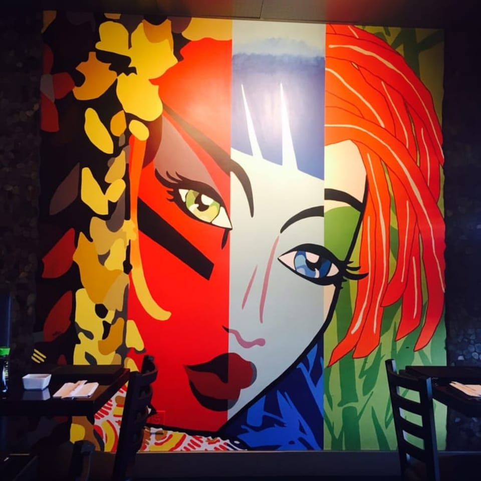 A vibrant, pop art style mural of a woman's face in bold colors adorns the restaurant wall.