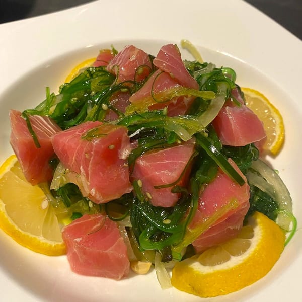 Close-up of a vibrant tuna poke salad with seaweed, onions, and lemon slices in a white bowl.