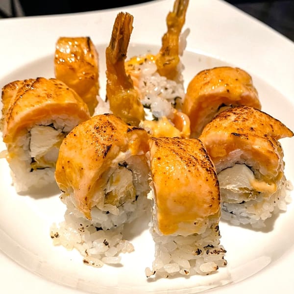 Sushi 4 Reel's salmon and shrimp tempura sushi rolls with creamy sauce on a white plate.