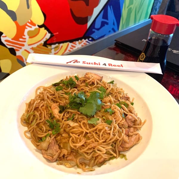 A plate of chicken chow mein with cilantro, chopsticks, and soy sauce on a table.